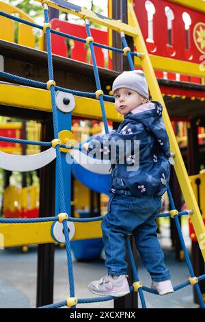 Ein Kind klettert in einem Park auf einem Spielplatz auf ein alpines Gitter. Kinderspielplatz in einem öffentlichen Park, Unterhaltung und Erholung für Kinder. Stockfoto