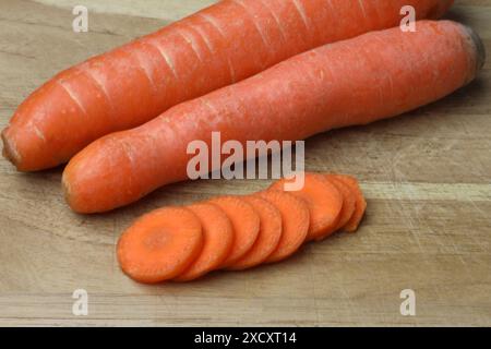 Eine Nahaufnahme von zwei ganzen Karotten und mehreren Karottenscheiben auf einem hölzernen Schneidebrett Stockfoto
