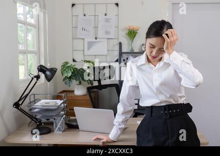 Geschäftsfrau, die in modernen Büroumgebungen mit Laptop und Dokumenten Kopfschmerzen hat Stockfoto