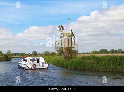 Ein Kreuzfahrtschiff auf dem River Ant, vorbei an der Turf Fen Drainage Mill im Sommer auf den Norfolk Broads am How Hill in Ludham, Norfolk, England, Großbritannien. Stockfoto