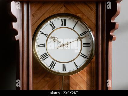 Eine antike, an der Wand montierte Großvateruhr aus Holz mit römischen Ziffern und einer Glastür auf einem schwach beleuchteten Innenhintergrund - 3D-Rendering Stockfoto