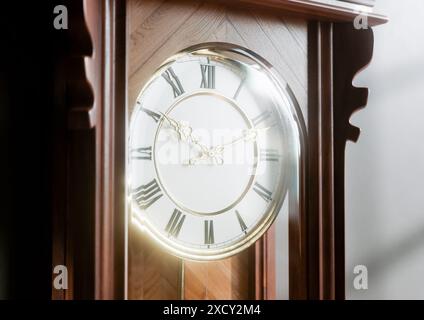 Eine antike, an der Wand montierte Großvateruhr aus Holz mit römischen Ziffern und einer Glastür auf einem schwach beleuchteten Innenhintergrund - 3D-Rendering Stockfoto