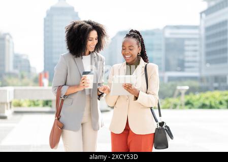 Zwei professionelle Schwarze Frauen diskutieren mit einem digitalen Tablet über Geschäfte im Außenbereich Stockfoto