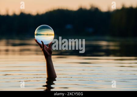 Hand einer Person, die eine Kristallkugel hält, die aus dem See ragt Stockfoto