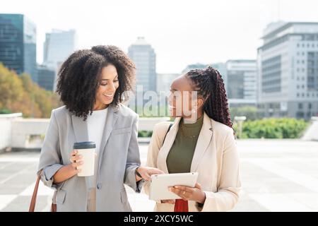 Zwei Schwarze Businessfrauen engagierten sich bei Outdoor-Meetings mit Tablet und Coffee in der Stadt Stockfoto
