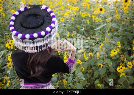 Eine junge Frau im Tribal-Outfit hebt ihre Hände, um ein herzförmiges Zeichen zu machen, das Liebe und Freundschaft vor dem Hintergrund eines wunderschönen Morgenflusses symbolisiert Stockfoto