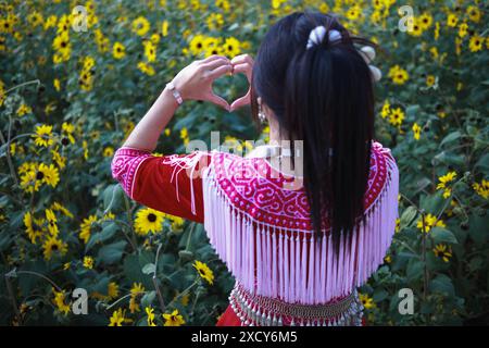 Eine junge Frau im Tribal-Outfit hebt ihre Hände, um ein herzförmiges Zeichen zu machen, das Liebe und Freundschaft vor dem Hintergrund eines wunderschönen Morgenflusses symbolisiert Stockfoto