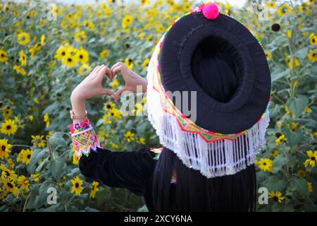 Eine junge Frau im Tribal-Outfit hebt ihre Hände, um ein herzförmiges Zeichen zu machen, das Liebe und Freundschaft vor dem Hintergrund eines wunderschönen Morgenflusses symbolisiert Stockfoto