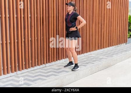 Frau, die eine Pause vom Joggen macht, in Sportbekleidung gegen einen Holzzaun steht. Stockfoto