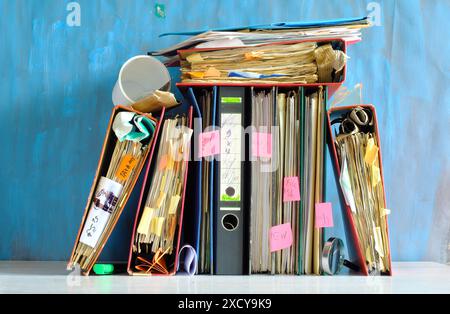 Unordentliche Aktenordner und Geschäftsunterlagen, Bürokratie, überarbeitet, übertroffen, übertroffen, schlagen das Uhrengeschäftskonzept auf grungy Blue Backgound. Stockfoto