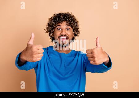 Foto von einem netten, positiven Kerl, der trendige blaue Kleidung trägt, mit Daumen nach oben isoliert auf beigefarbenem Hintergrund Stockfoto