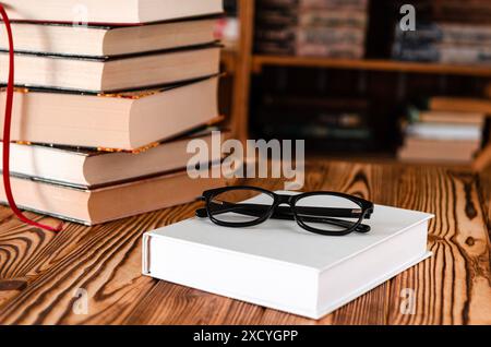 Schwarze Gläser liegen auf einem weißen Buch neben alten Büchern vor dem Hintergrund von Bücherregalen Stockfoto