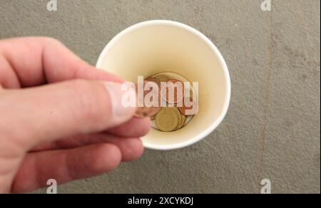 Ein Mann wirft eine zwei-Cent-Münze in einem Pappbecher, in dem bereits einige Münzen sind. Symbolbild/Symbolfoto Bettler/betteln. Schnelsen Hamburg *** Ein Mann wirft eine zwei-Cent-Münze in einen Pappbecher, der bereits einige Münzen enthält symbolisches Bild symbolisches Foto Beggar Betteln Schnelsen Hamburg Stockfoto
