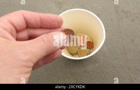 Ein Mann wirft eine zwei-Cent-Münze in einem Pappbecher, in dem bereits einige Münzen sind. Symbolbild/Symbolfoto Bettler/betteln. Schnelsen Hamburg *** Ein Mann wirft eine zwei-Cent-Münze in einen Pappbecher, der bereits einige Münzen enthält symbolisches Bild symbolisches Foto Beggar Betteln Schnelsen Hamburg Stockfoto