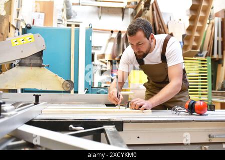 Freundlich Tischler mit Gehörschutz und Arbeitskleidung arbeiten an einer Säge in der Werkstatt Stockfoto