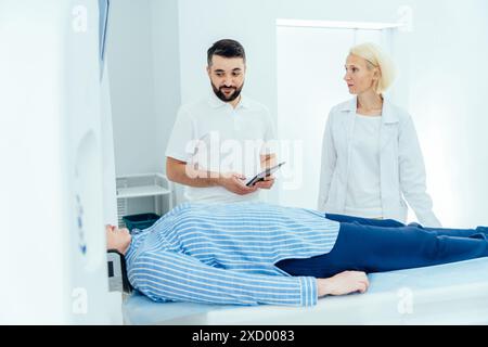 Der Mann steht neben einer Frau, die auf einem Tisch liegt. Der Mann hält ein Klemmbrett und sieht die Frau an. Die Frau trägt einen weißen Mantel Stockfoto