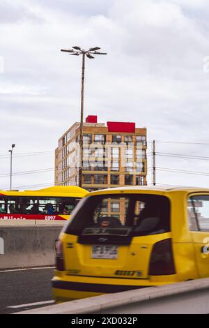 Gelbes Taxi und TransMilenio-Bus in einer Bogotá-Straße mit einem modernen Apartmentgebäude im Hintergrund an einem bewölkten Tag Stockfoto