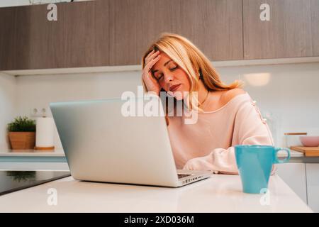 Eine hart arbeitende Frau, verzweifelt wegen Laptop-Problemen, die Stress und Kopfschmerzen verursachen. Eine frustrierte Frau, die mit übermäßiger Arbeit zu tun hat, die Angst und Migräne auslöst. Jobprobleme. Hochwertige Fotos Stockfoto