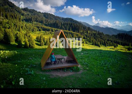 Touristen Wanderer Frau in blauer Jacke Rast in Sommerhaus mit Dreieckdach an Luftdrohne schöne Landschaft mit wilden Berg- und Fichtenvordern Stockfoto