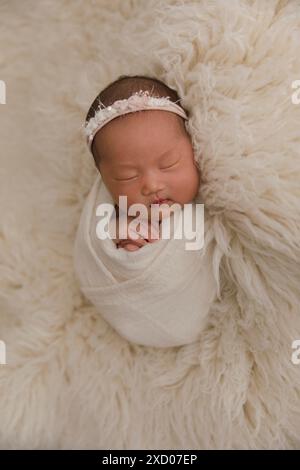 Blick von oben auf ein neugeborenes Baby, das auf einem Bett unter beiger Decke schläft und eine biegsame Stirnband-Blume auf ihrem Kopf. Kopierbereich. Neugeborene-Pflegekonzept. Stockfoto