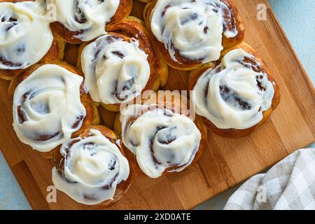 Zimtbrötchen, hausgemachte traditionelle süße Brötchen mit Frischkäse auf Holzbrett Stockfoto