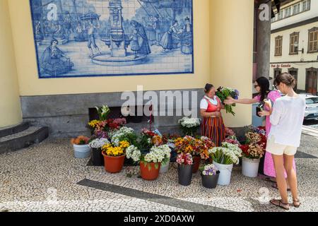 Blumenfrau in rotem Wollrock und weißer Bluse verkauft einen Blumenstrauß an der Straßenecke auf dem Bauernmarkt. Stockfoto