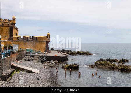 Die Menschen schwimmen am Strand vor der Festung São Tiago in Funchal. Stockfoto