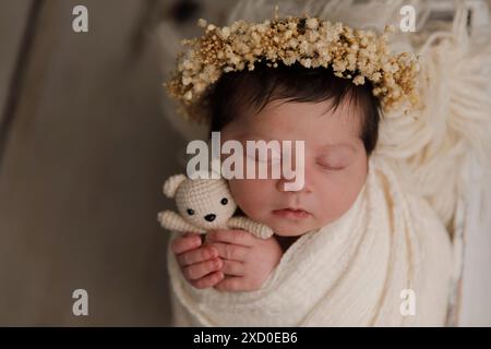 Blick von oben auf ein neugeborenes Baby, das auf einem Bett unter beiger Decke schläft und eine biegsame Stirnband-Blume auf ihrem Kopf. Kopierbereich. Neugeborene-Pflegekonzept. Stockfoto