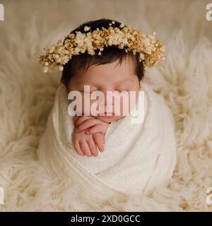 Blick von oben auf ein neugeborenes Baby, das auf einem Bett unter beiger Decke schläft und eine biegsame Stirnband-Blume auf ihrem Kopf. Kopierbereich. Neugeborene-Pflegekonzept. Stockfoto