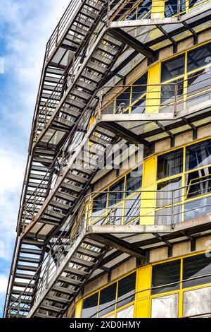 Ein antikes Industriegebäude mit markanten Nottreppen und großen gelben Fenstern, das sein historisches architektonisches Design zeigt. Stockfoto