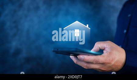 Eine Person hält ein Handy mit einem Haus auf dem Bildschirm. Das Haus ist beleuchtet und er leuchtet. Stockfoto