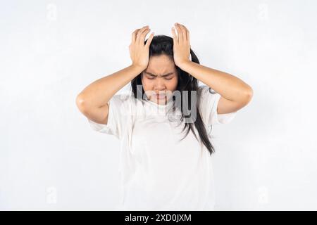 Eine Frau mit den Händen auf dem Kopf, die sehr verärgert aussieht. Sie trägt ein weißes Hemd Stockfoto