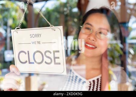 Kaukasische Frau, die ein Schild von offen zu geschlossen an der Eingangstür seines kleinen Cafés dreht. Aus dem Geschäft Stockfoto