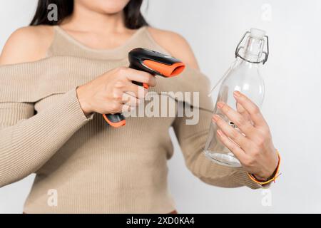 Eine Frau hält eine Flasche und einen Strichcode-Scanner in der Hand. Sie trägt ein braunes Hemd. Das Konzept der Neugier und Erkundung, da die Frau den Barcode benutzt Stockfoto