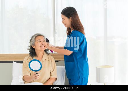 Eine Frau in blauer Uniform hilft einer älteren Frau mit ihren Haaren. Pflegekraft, Pflegeassistent, Seniorenkonzept. Stockfoto