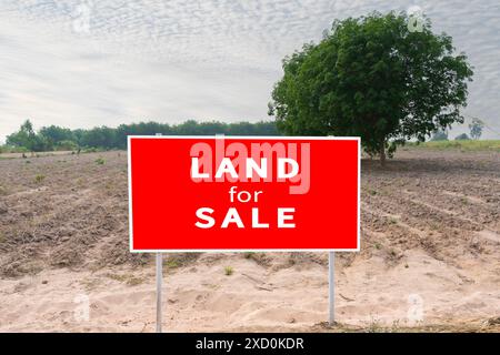 Ein rotes Schild mit der Aufschrift „Land zum Verkauf“ steht auf einem Feldfeld. Das Schild ist von einem weißen Hintergrund umgeben. Stockfoto