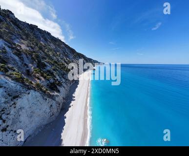 Aus der Vogelperspektive auf einen unberührten Strand mit türkisfarbenem Wasser und einer zerklüfteten Klippe unter einem klaren blauen Himmel in Lefkada, Griechenland Stockfoto