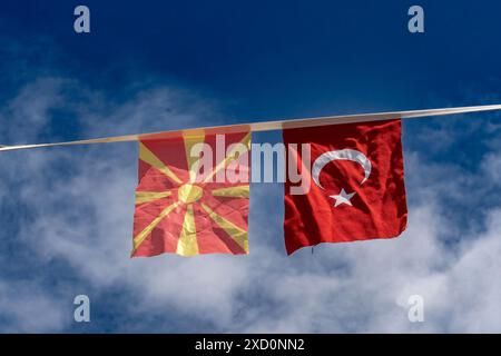 Einheit in Vielfalt. Die Fahnen der Türkei und Mazedoniens hängen zusammen. Blauer Himmel mit Wolken als Hintergrund. Stockfoto