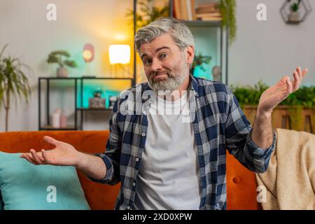 Ich weiß nicht, was ich sagen soll. Verwirrter, ranghärtiger Mann, der sich über zweideutige Fragen peinlich fühlt und Zweifel hat, keine Ahnung, dass er zu Hause ahnungslos und unsicher ist. Ein reifer Kerl sitzt auf dem Sofa im Wohnzimmer. Stockfoto
