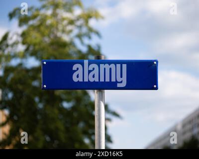 Leeres Straßennamensschild als Vorlage und Kopierbereich. Blaue Metallplatte vor einem Baum und dem Himmel. Positionierungshilfe, die die Richtung anzeigt. Stockfoto