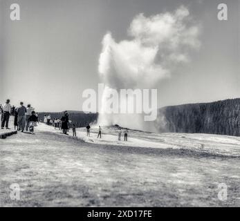 Horizontale Schwarzweißaufnahme von Touristen in den späten 1940er Jahren, die Old Faithful beim Ausbruch beobachteten. Stockfoto