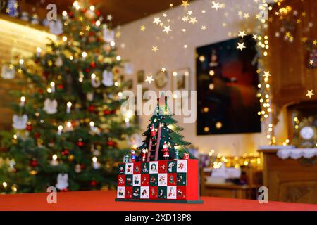 Gemalter Adventskalender aus Holz mit stilisiertem Weihnachtsbaum, winzigen Figuren und Schubladen, die auf einem Tisch inmitten eines weihnachtlichen Dekors stehen Stockfoto