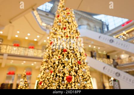 Verschwommener Blick auf einen riesigen Weihnachtsbaum in der zentralen Halle eines großen Einkaufszentrums, mit großen Weihnachtskugeln und vielen LED-Lichtern, Multi-Lev Stockfoto