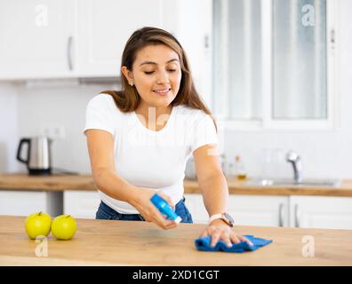 Lächelnde junge hispanische Frau, die zu Hause Küchenoberflächen abwischt Stockfoto