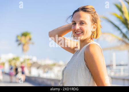 Eine junge rothaarige Frau mit weißem Tanktop lächelt an einem Sommertag in die Kamera. Stockfoto