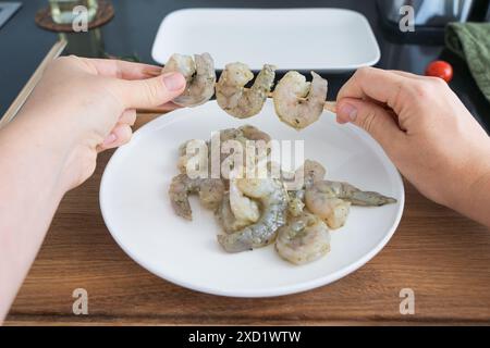 Nahaufnahme der Hände, die gewürzte rohe Garnelen oder Bambusstäbchen spießen, Garnelen grillen. Rezept für Meeresfrüchte, Garnelen Stockfoto