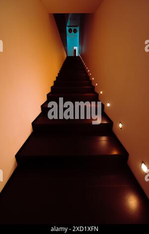 Eine vertikale, dezente Aufnahme einer modernen, schwach beleuchteten Treppe mit dunklen Holztreppen und kleinen quadratischen Lichtern in den Wänden auf beiden Seiten. Die Stai Stockfoto