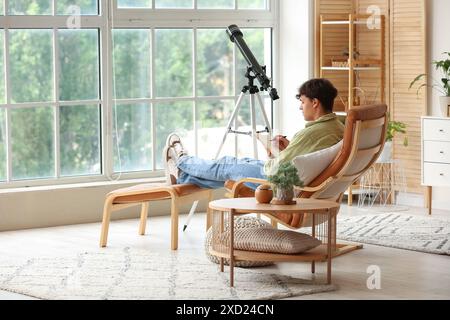 Junger Mann mit Teleskop und Notizbuch, der im Sessel sitzt Stockfoto