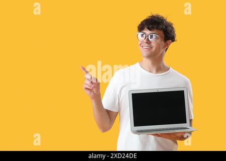 Männlicher Programmierer mit leerem Laptop, der auf etwas auf gelbem Hintergrund zeigt Stockfoto