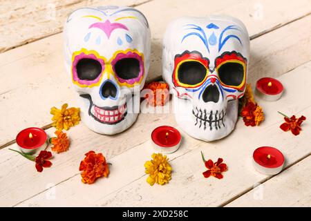 Bemalte menschliche Schädel mit brennenden Kerzen und wunderschönen Blumen für Mexikos Tag der Toten auf weißem Holztisch Stockfoto